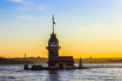 Lighthouse by sea against sky during sunset