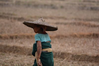 Rear view of woman wearing asian style conical hat on field