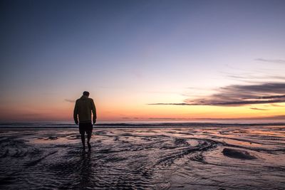 Rear view of silhouette man walking on beach at sunset