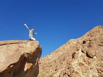Low angle view of man climbing rock against clear blue sky