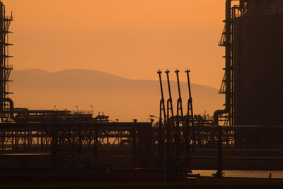 Silhouette cranes on pier against sky during sunset