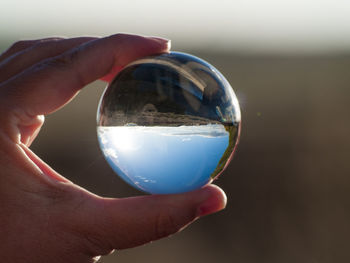 Close-up of hand holding crystal ball against sky