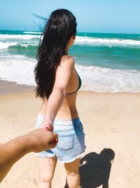 Close-up of man holding hand of woman at beach against sky