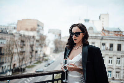 Young woman wearing sunglasses standing against cityscape