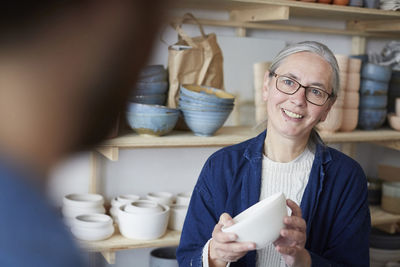 Smiling mature woman discussing with man over bowl in pottery class