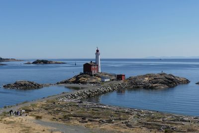 Lighthouse by sea against clear sky