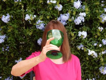Portrait of woman holding large green glass against flowering plants