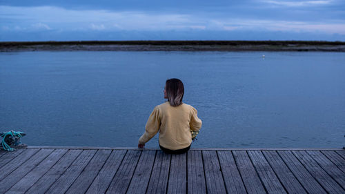 Rear view of woman sitting on pier against sky