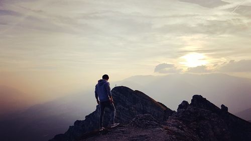 Man sitting on rock against sky
