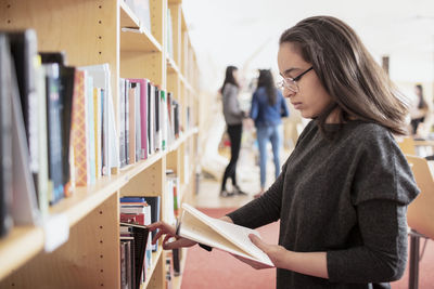 Teenage girl reading book near bookshelf