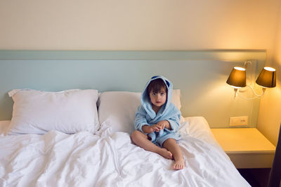 Baby boy two years old in a blue terry robe with a hood lying on a big bed