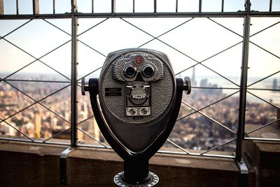 Coin-operated binoculars by cityscape against sky