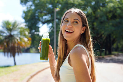 Attractive brazilian sporty girl holding green smoothie detox juice outdoors