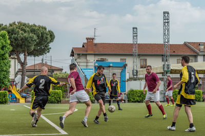 Rear view of people playing on soccer field against sky