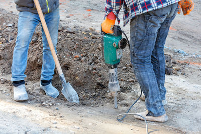 Workers loosen the sandy soil with an electric jackhammer at the workplace.