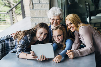 Sisters taking selfie with mother and grandmother through tablet computer on porch