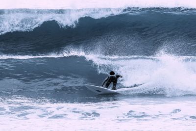 Rear view of person surfing by waves in sea