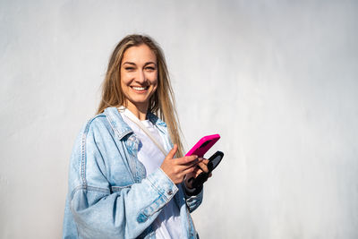 Portrait of young woman using mobile phone while standing against wall