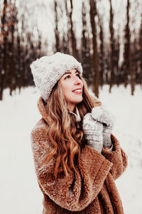 Portrait of young woman standing against trees during winter
