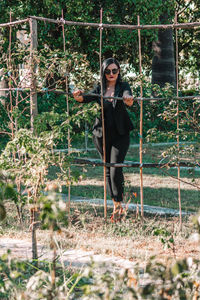Portrait of female model standing behind fence at park