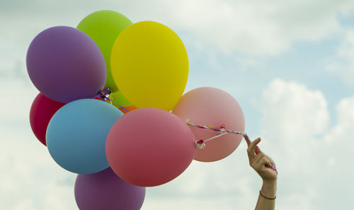 Close-up of hand holding balloons against sky