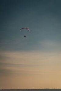 Low angle view of person paragliding against sky during sunset