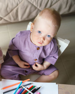 Cute blue eyed baby boy with golden hair looking at camera while playing at home