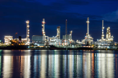 Illuminated factory by river against sky at night