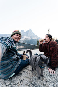 Young couple enjoys a time in wilderness taking selfies laughing and having fun with their gray cat