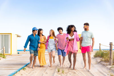 Rear view of friends standing at beach against clear sky