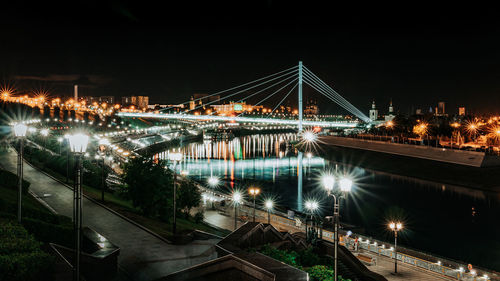 Illuminated bridge over river against sky at night