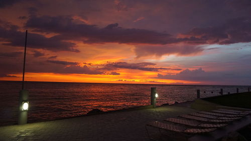 Promenade by sea against cloudy sky during sunset