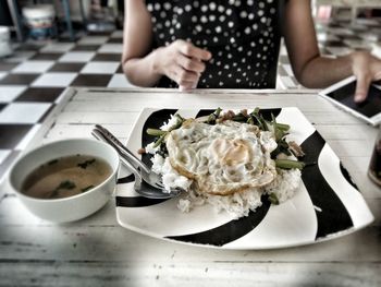 Midsection of woman sitting by food in plate on table