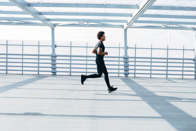 Side view of young man running on footbridge