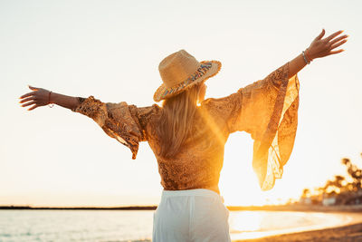 Rear view of woman with arms raised standing at beach