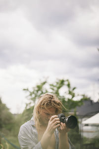 Portrait of woman photographing against sky