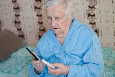 Portrait of a 90-year-old sick pensioner who holds a package of pills and a phone in her hands.