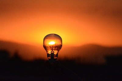 Close-up of light bulb against orange sky during sunset