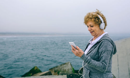 Woman listening music at beach against sky