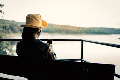 Man sitting on boat looking at lake against sky