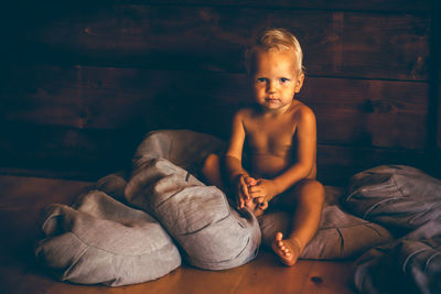 Portrait of shirtless baby boy with cushions sitting on floor at home