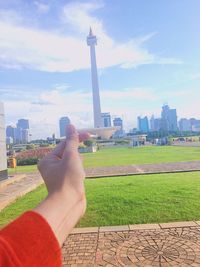 Cropped image of person hand by cityscape against sky