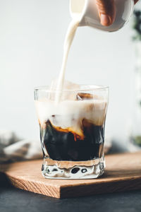 Close-up of hand pouring milk in coffee cup on table