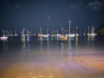 Sailboats moored on harbor against sky at night