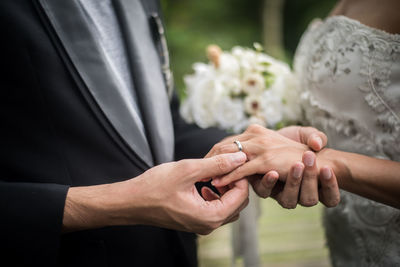 Midsection of bride and groom exchanging rings while holding hands