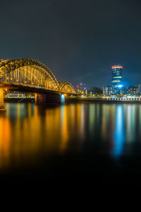 Illuminated bridge over river with buildings in background