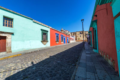 Walkway amidst residential buildings against clear blue sky