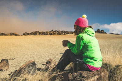 Rear view of woman sitting on land against sky