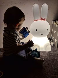 Side view of baby sitting with toy at home