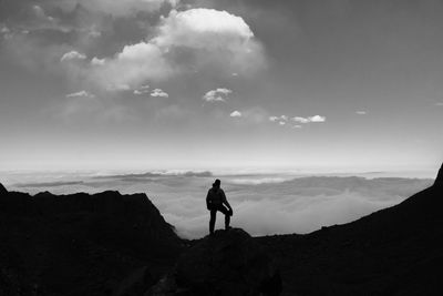 Silhouette man standing on rock against sky